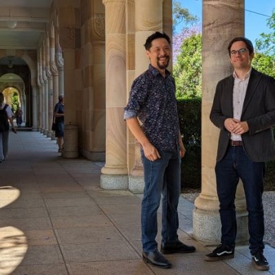 two  men stand by a pillar in a shady stone walkway